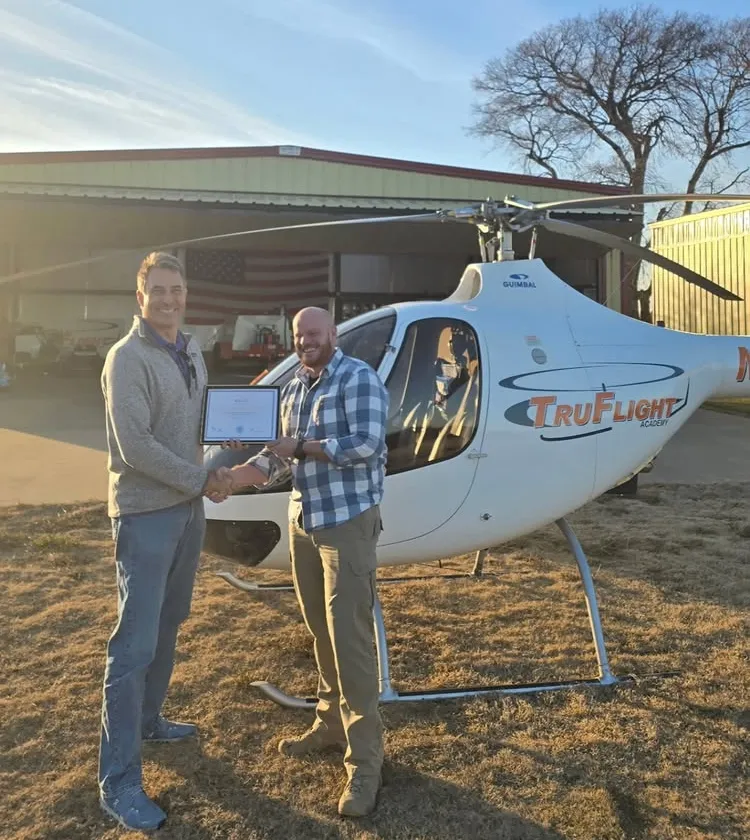 Student and instructor smiling and holding certificate in front of a helicopter