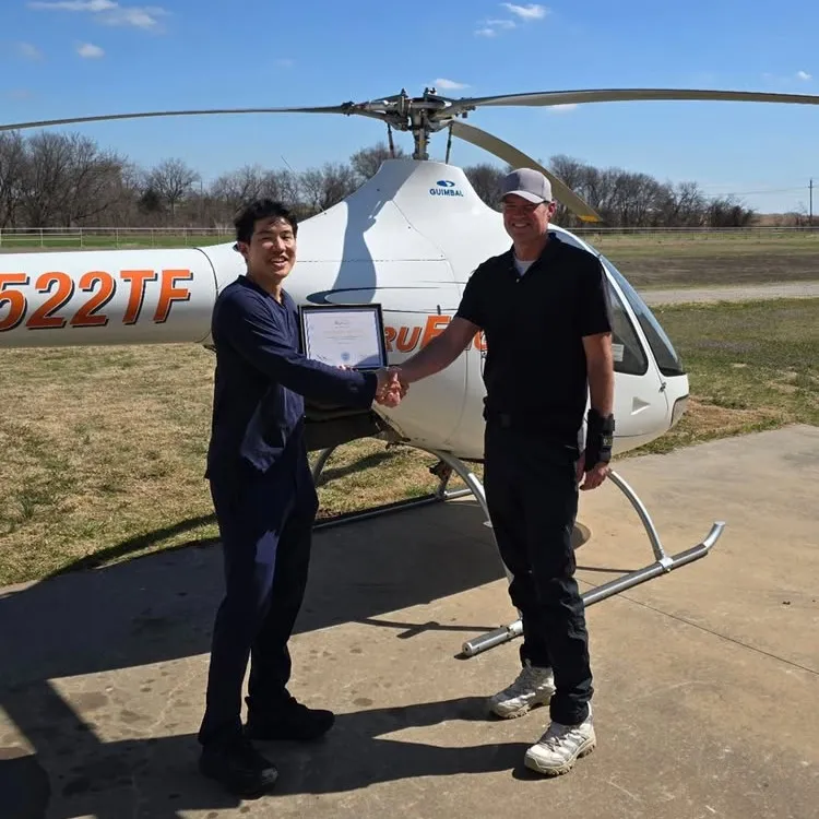 Student and instructor smiling and holding certificate in front of a helicopter