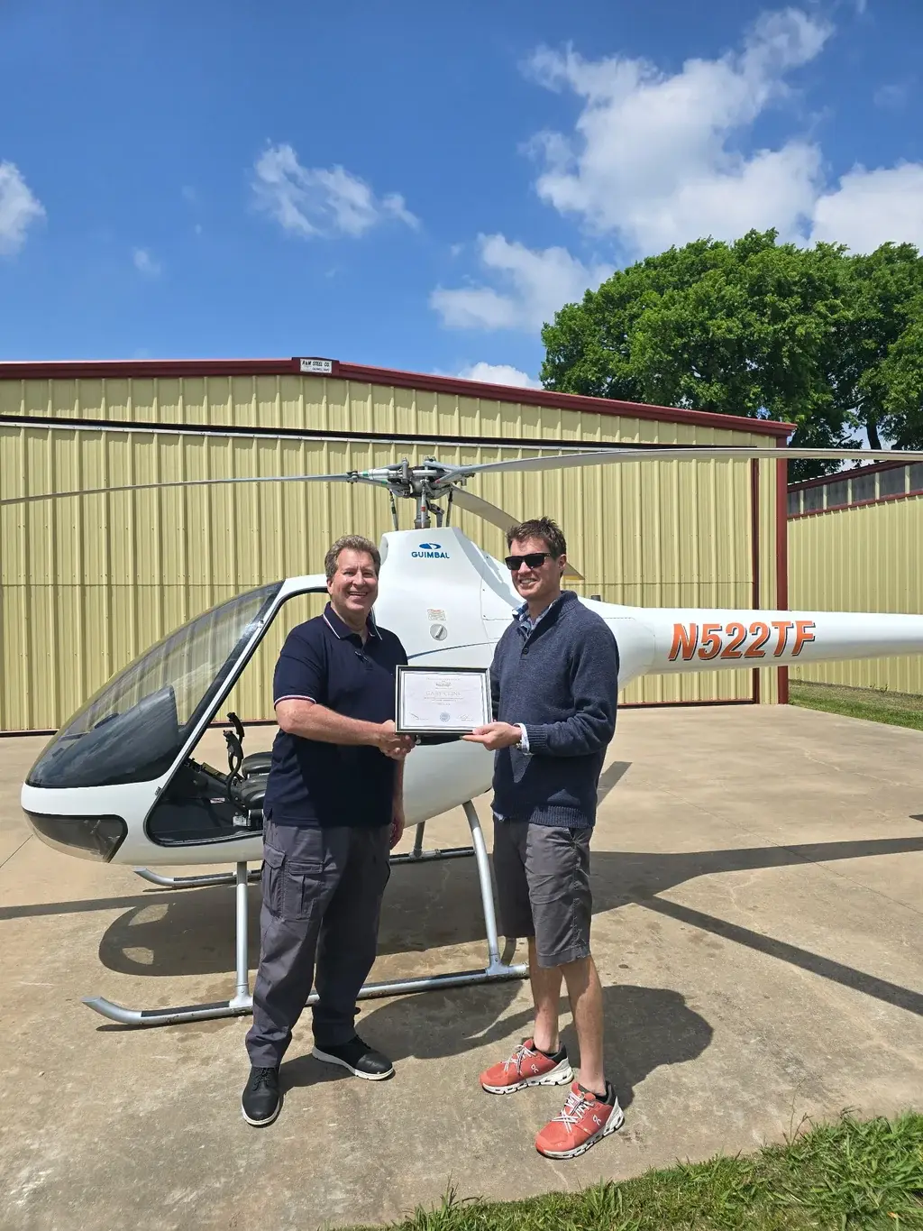 Student and instructor holding certificate in front of helicopter