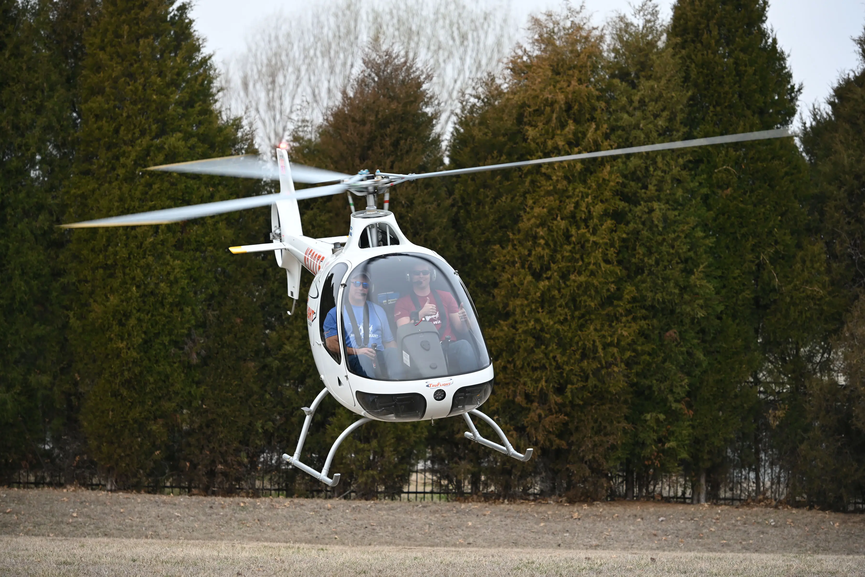 Helicopter taking off with one of the pilot giving a thumbs up and trees in the background