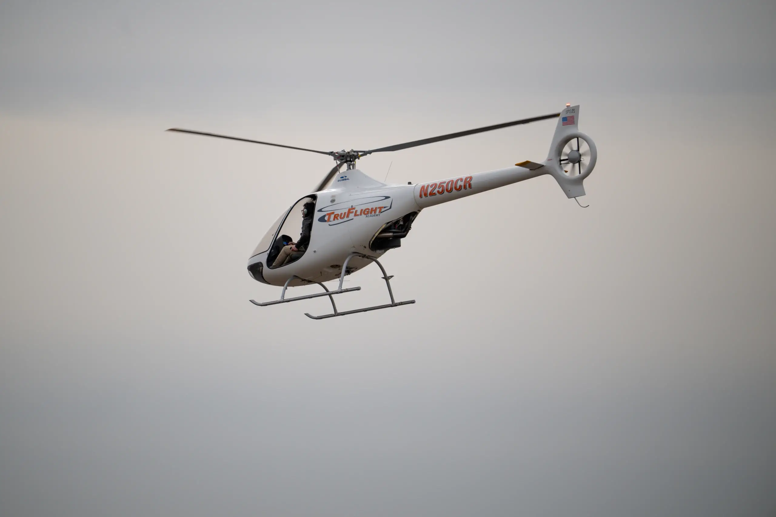 TruFlight Academy Guimbal Cabri G2 helicopter in flight against a pale hazy sky