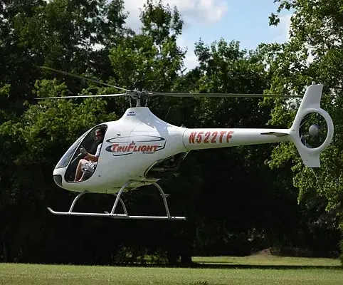 TruFlight Academy Guimbal Cabri G2 hovering low in front of dense green trees