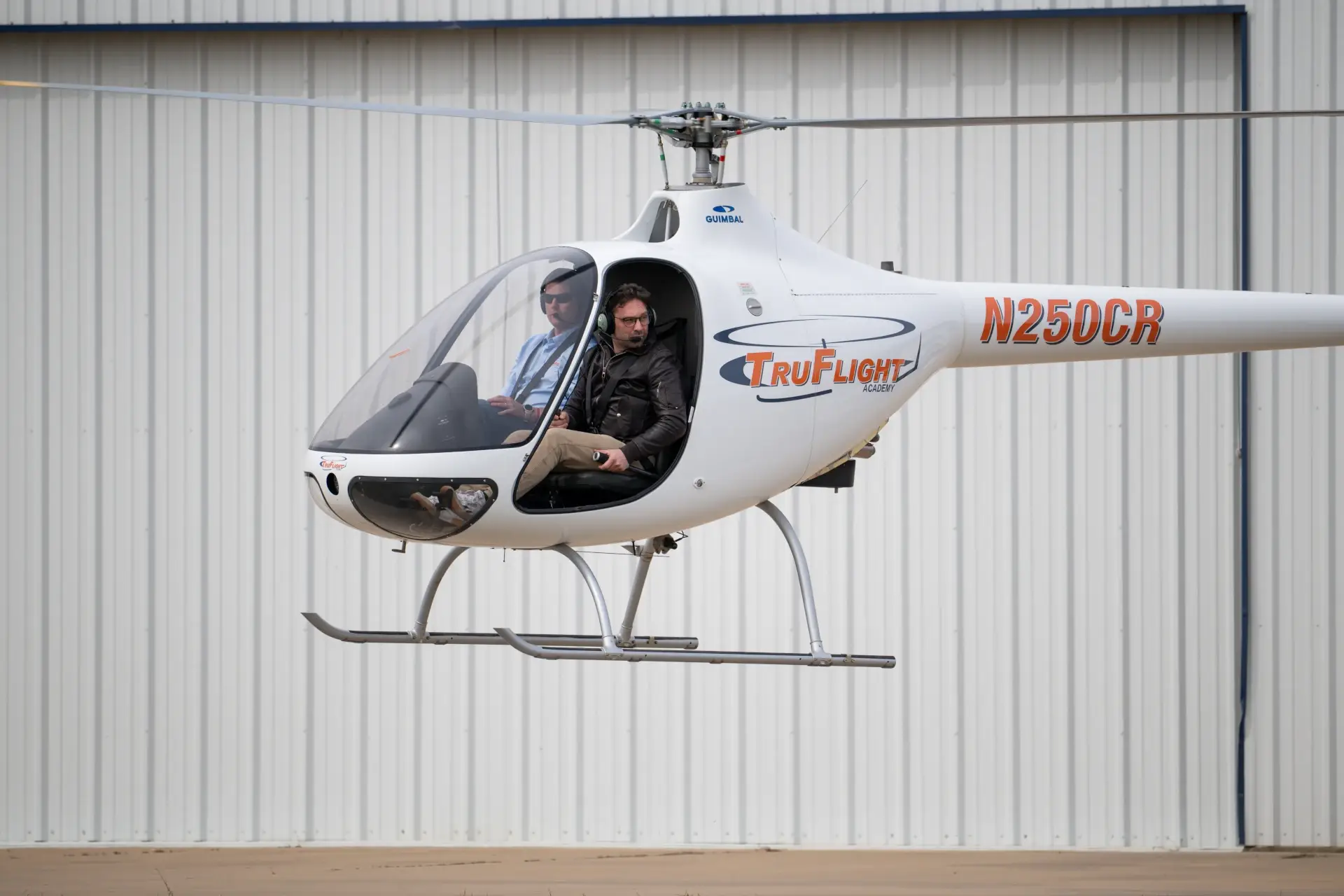 Side view of two pilots inside hovering TruFlight Academy's helicopter