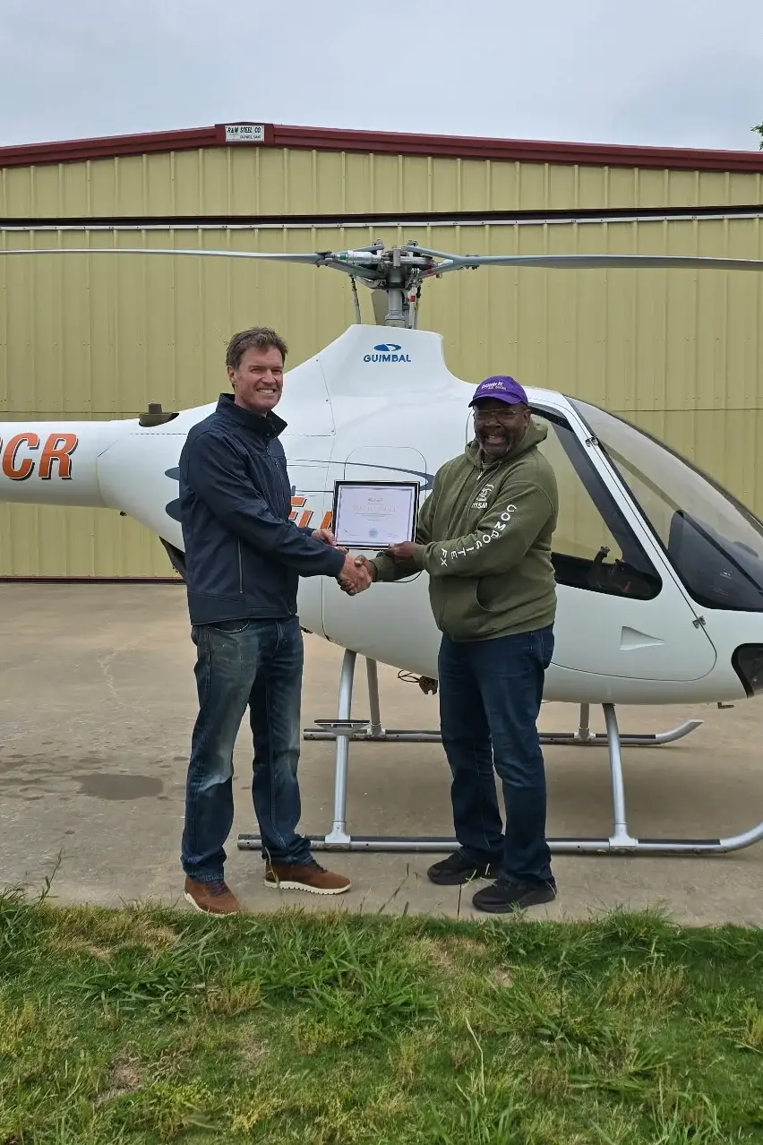 Student and instructor shaking hands and holding certificate in front of helicopter