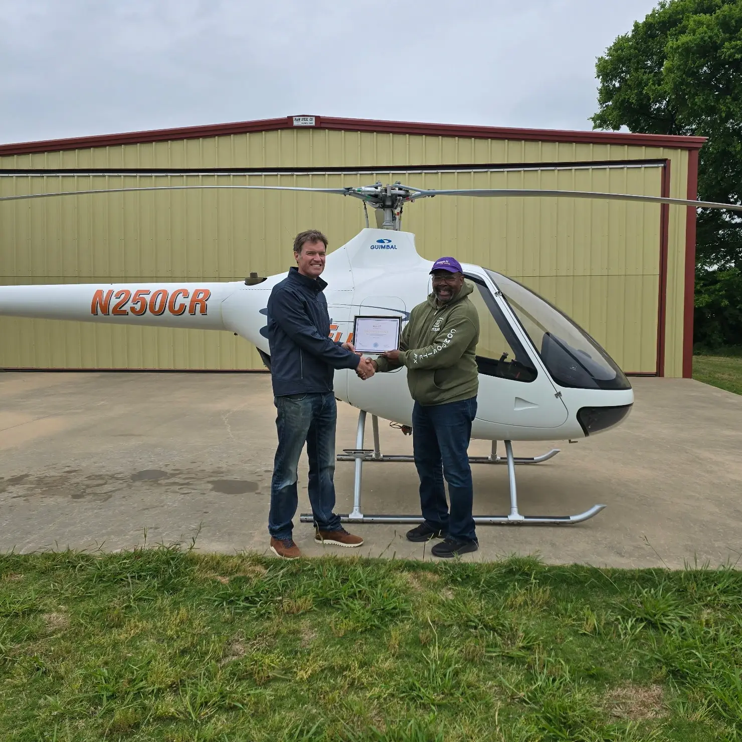 Student and instructor shaking hands and holding certificate in front of helicopter