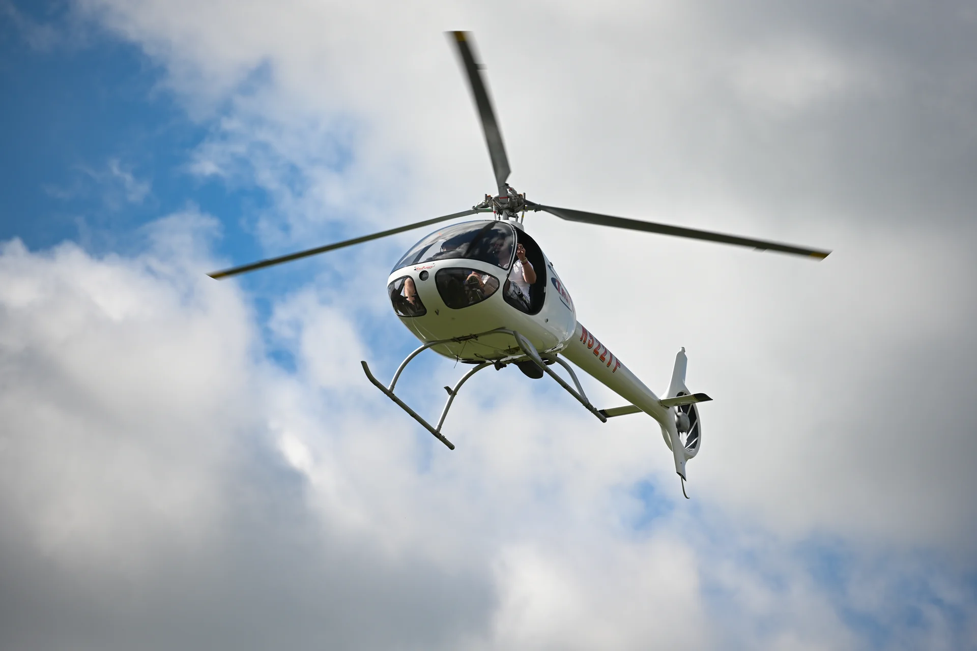 TruFlight Academy Cabri G2 helicopter in flight with a passenger waving from the open side window