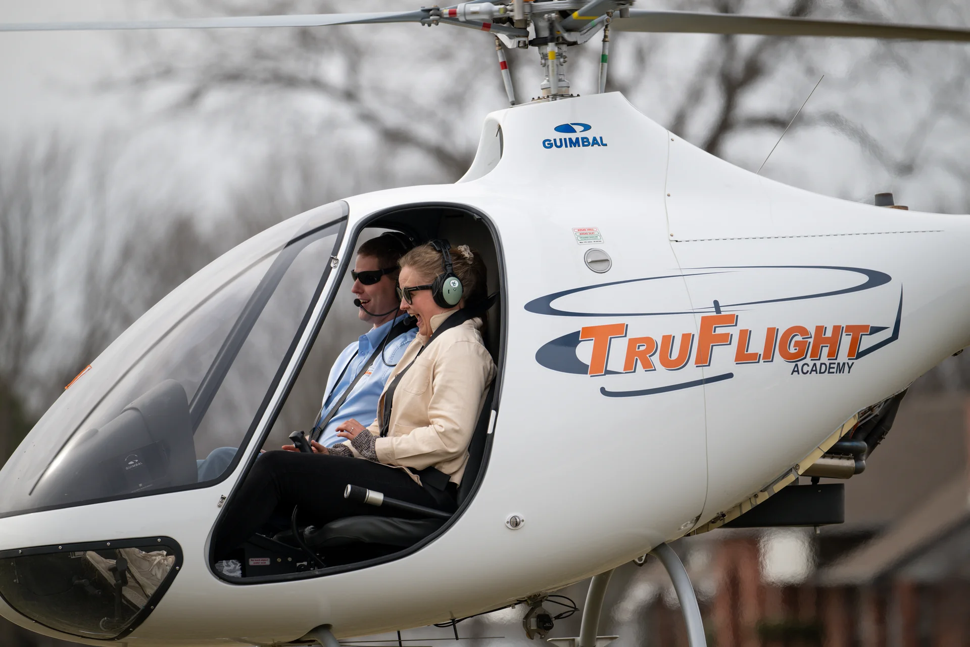 Two people wearing headsets seated in the cockpit of a TruFlight Academy Guimbal helicopter