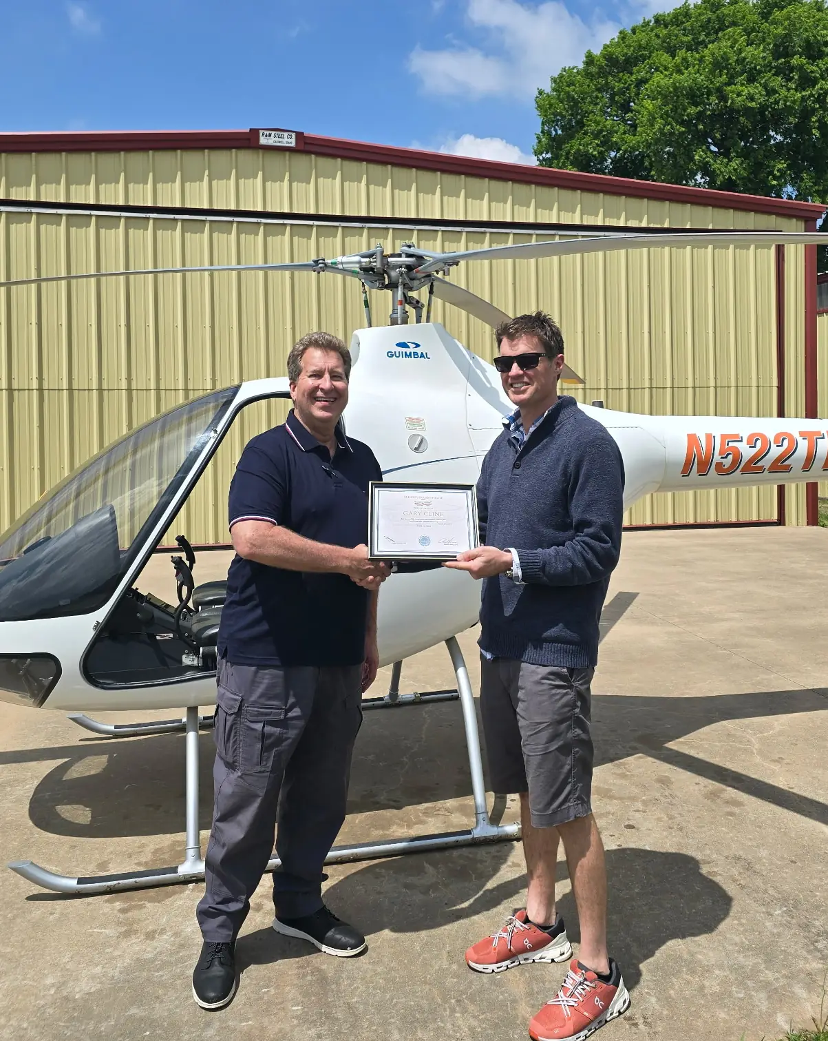 Student and instructor holding certificate in front of helicopter