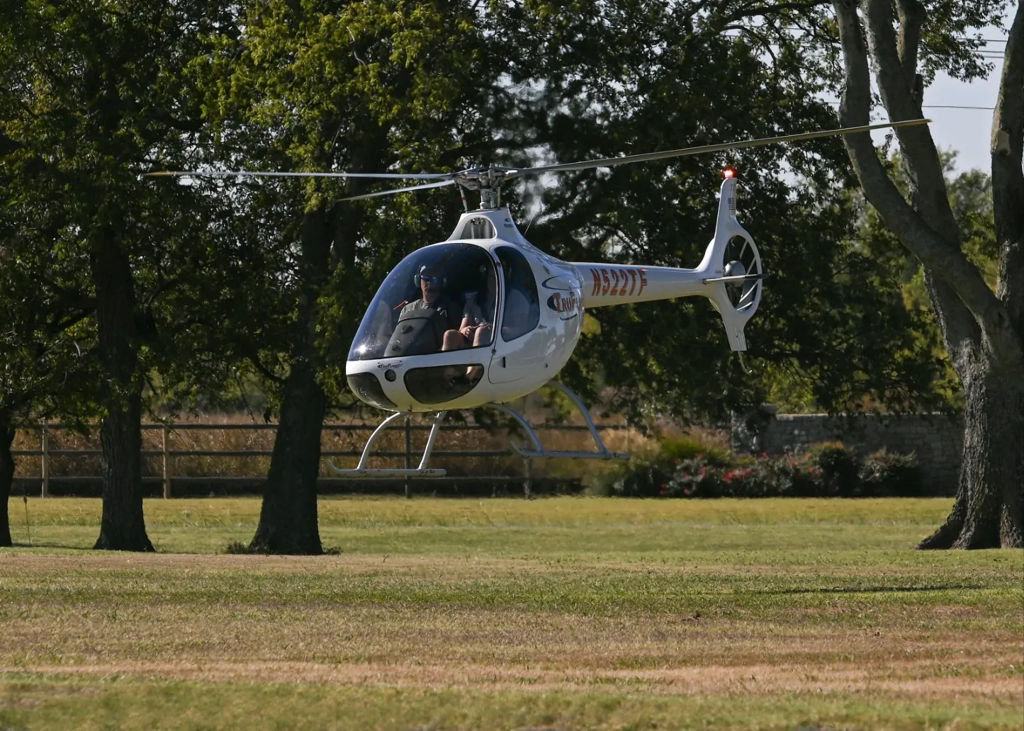 Cabri G2 helicopter hovering over a grass field with trees behind it